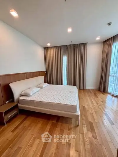 Spacious bedroom with wooden flooring and large windows in modern apartment.