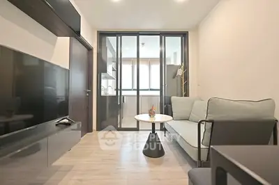 Modern living room with sleek furniture and glass partition leading to kitchen area.