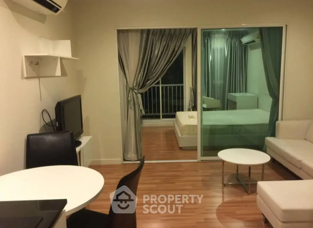 Modern apartment with open living room and bedroom, featuring sleek furniture and wooden flooring.
