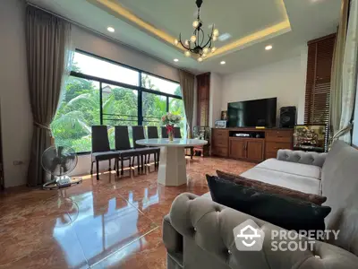 Spacious living room with polished marble floors, elegant chandelier, and large windows offering a lush garden view, perfect for entertaining guests.