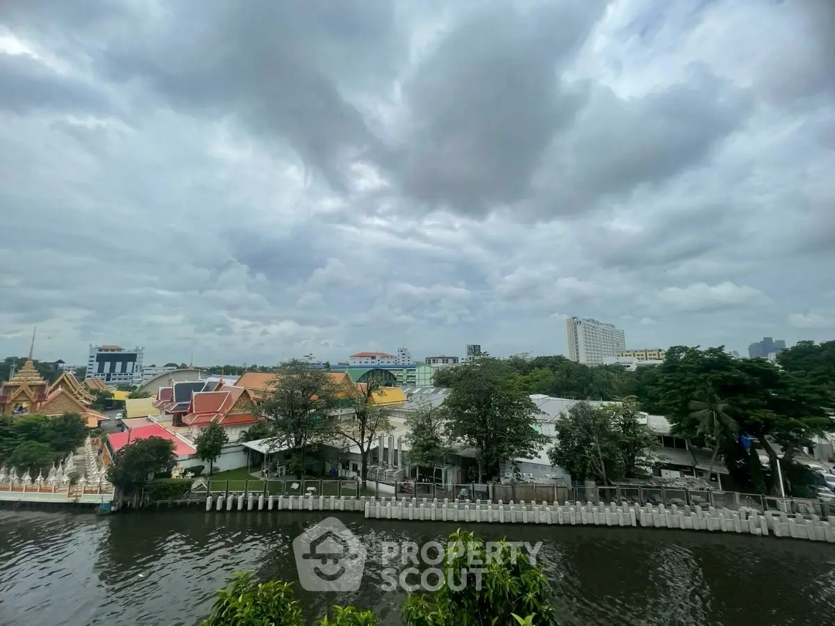 Scenic river view with colorful buildings and lush greenery under a cloudy sky.