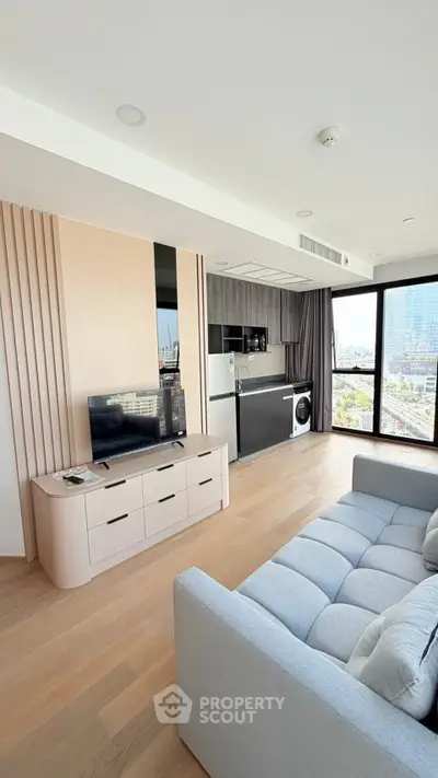 Modern living room with open kitchen and city view, featuring sleek furniture and natural light.