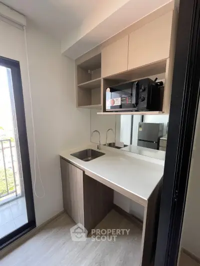 Modern kitchen with sleek cabinetry and balcony view, featuring a compact design and natural light.