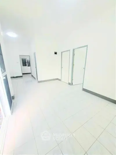 Spacious and bright interior with white tiled flooring and multiple doorways.