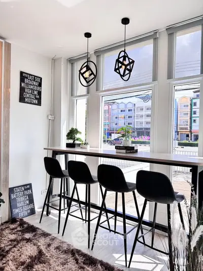 Modern dining area with high stools and large windows, featuring stylish pendant lights.