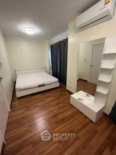 Cozy bedroom with wooden flooring and modern furnishings, featuring a comfortable bed and sleek mirror.