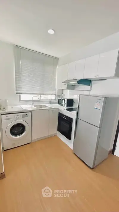 Modern kitchen with sleek appliances and ample natural light, featuring a washing machine and oven.