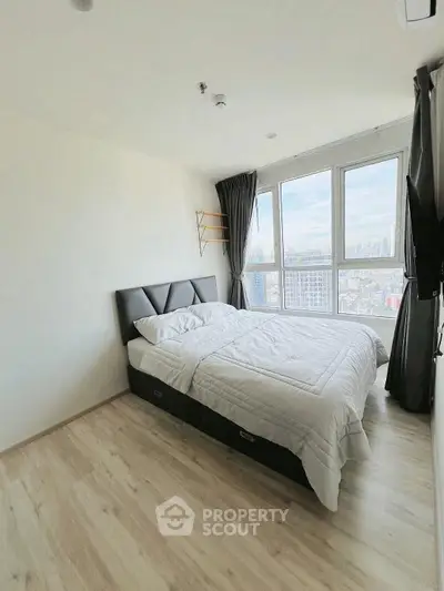 Modern bedroom with city view and natural light in high-rise apartment.
