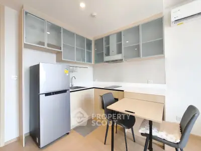 Modern kitchen with sleek cabinets, dining table, and stainless steel fridge in a cozy apartment.