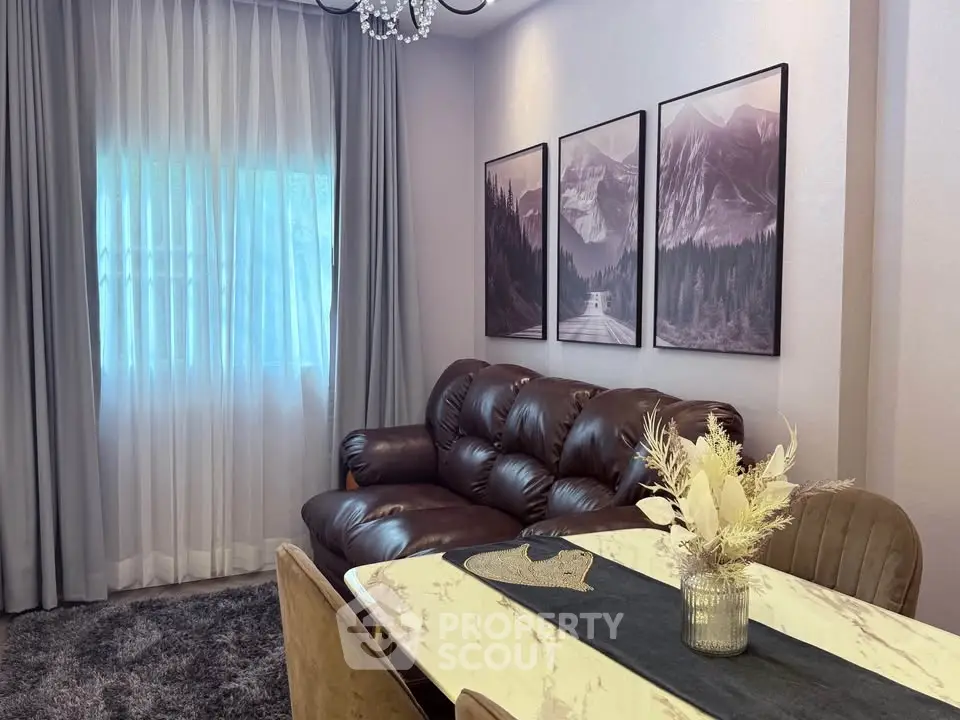 Elegant living room with plush leather sofa, chic decor, and natural light through sheer curtains.