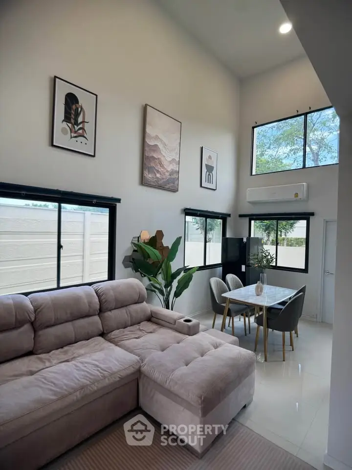 Modern living room with high ceilings, stylish decor, and large windows offering natural light.