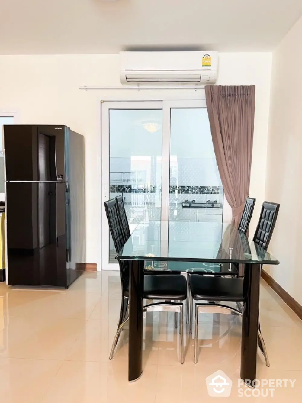 Modern dining area with sleek black chairs and glass table, complemented by a large fridge and natural light from balcony doors.