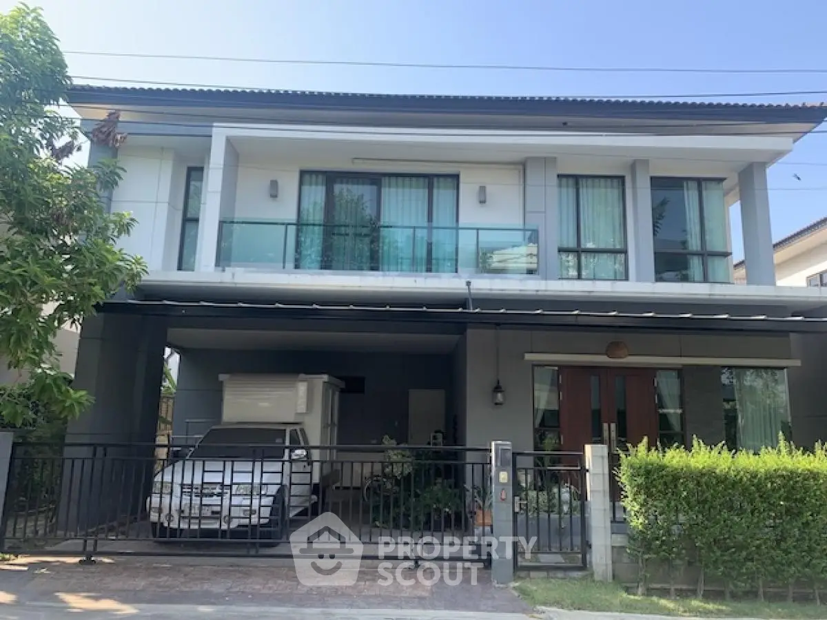 Modern two-story house with balcony and gated driveway in a suburban neighborhood.