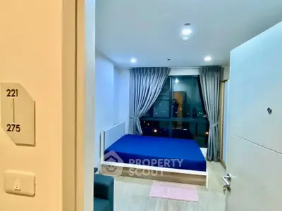 Modern bedroom with city view, featuring a blue bedspread and elegant curtains, perfect for urban living.
