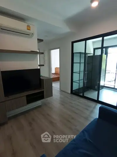 Modern living room with sleek design and large glass doors leading to a balcony, featuring a TV and air conditioning.