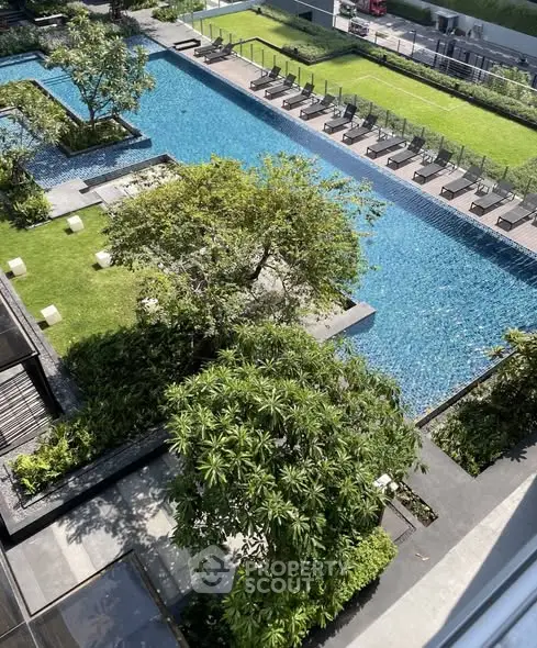 Luxurious rooftop pool with lush greenery and sun loungers in a modern apartment complex.