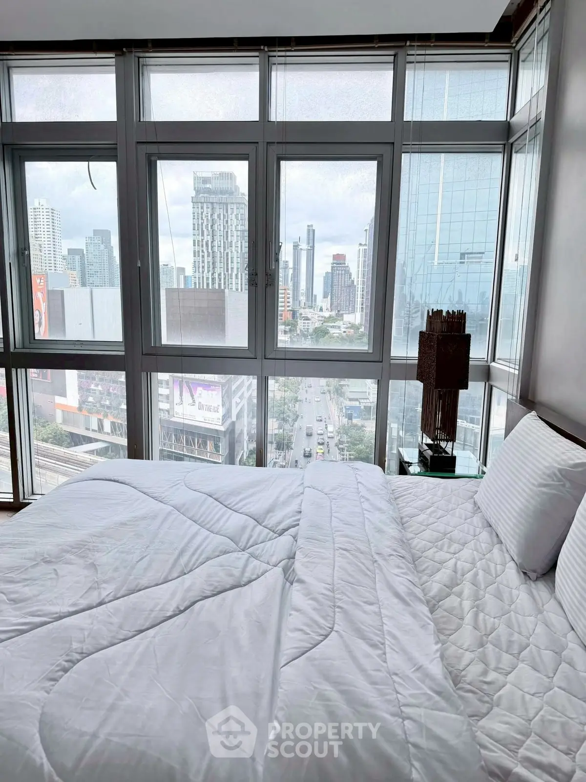Luxurious bedroom with stunning city view from large windows in modern high-rise apartment.