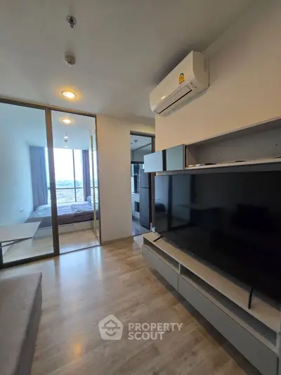 Modern apartment interior with sleek design and large TV, featuring a glimpse of the bedroom.