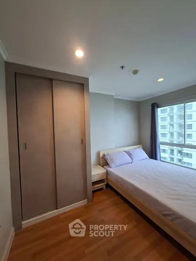 Cozy bedroom with wooden flooring and large window offering city view