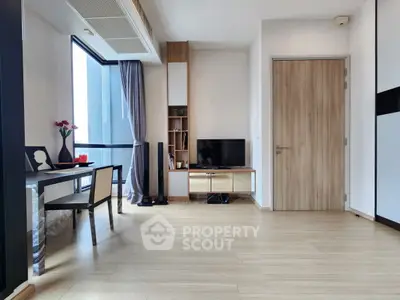 Modern living room with wooden flooring, TV setup, and dining area near large window.