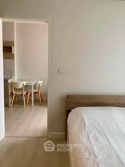Modern bedroom with wooden bed frame and view into minimalist kitchen area.