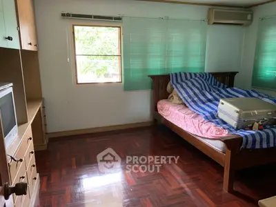 Cozy bedroom with wooden flooring and ample natural light, featuring a bed and built-in storage.