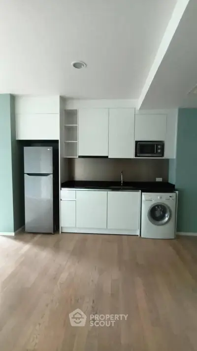 Modern kitchen with sleek cabinets, fridge, microwave, and washing machine in open layout.