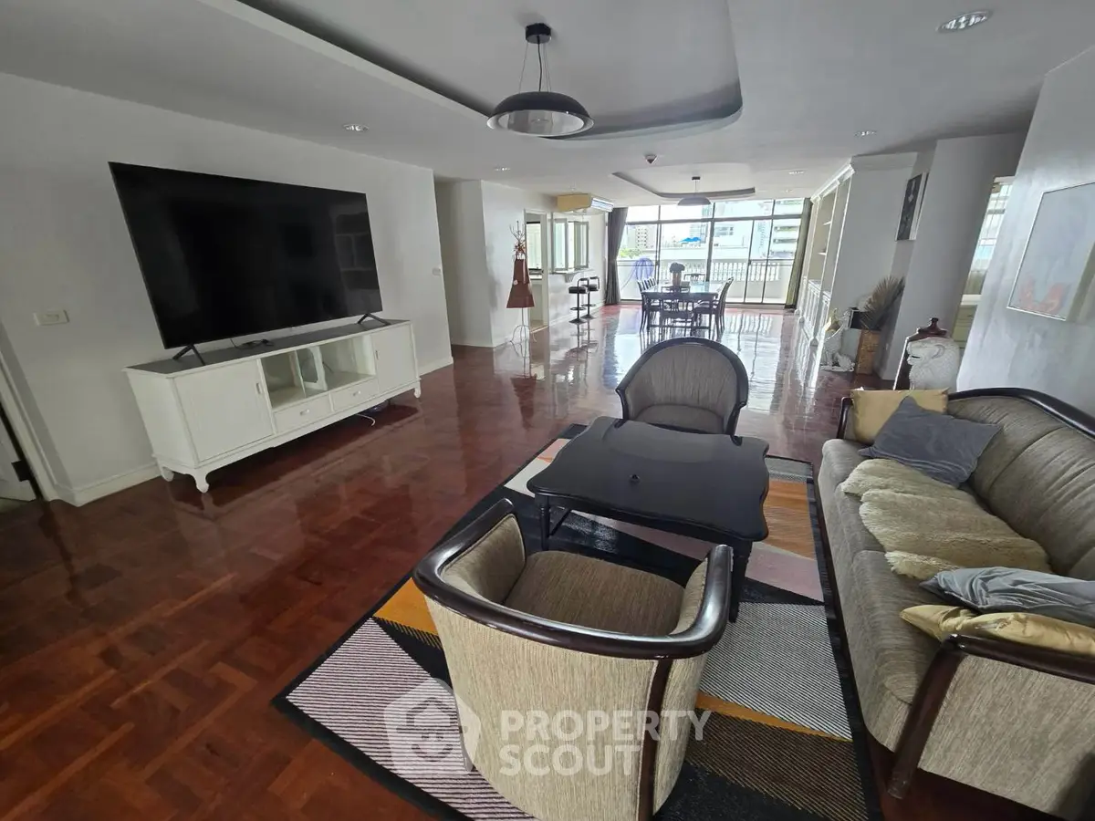 Spacious living room with elegant furniture and large TV, featuring polished wooden floors and ample natural light.