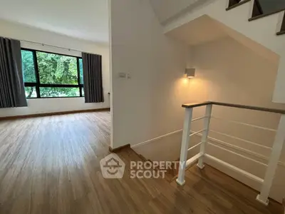 Spacious living area with wooden flooring and large window overlooking greenery.