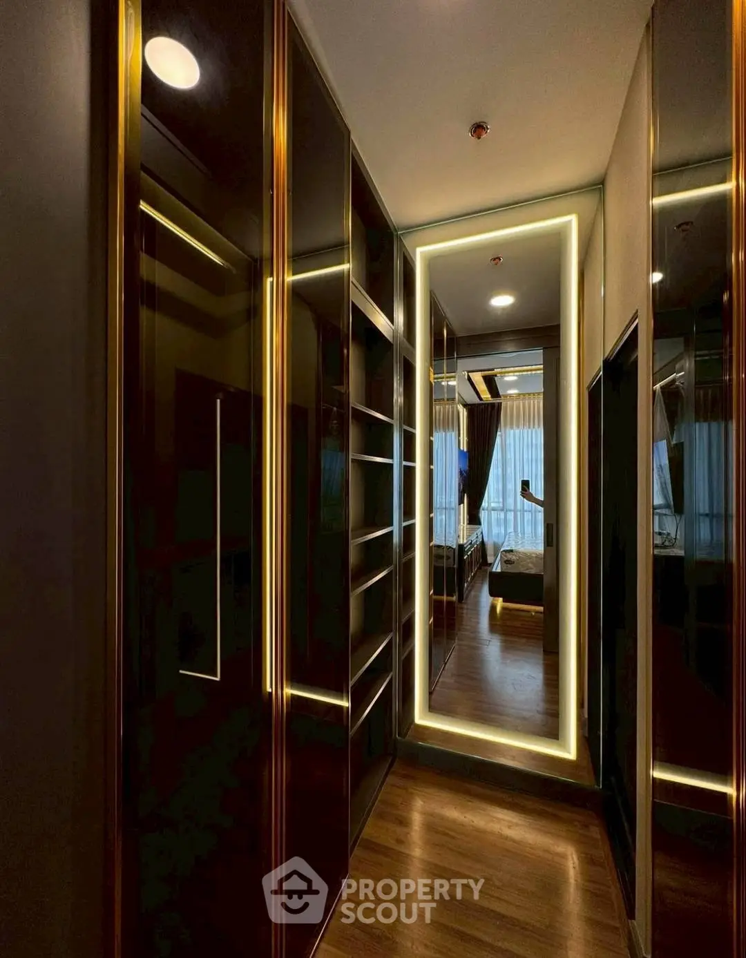 Luxurious walk-in closet with elegant lighting and mirrored accents leading to a stylish bedroom.