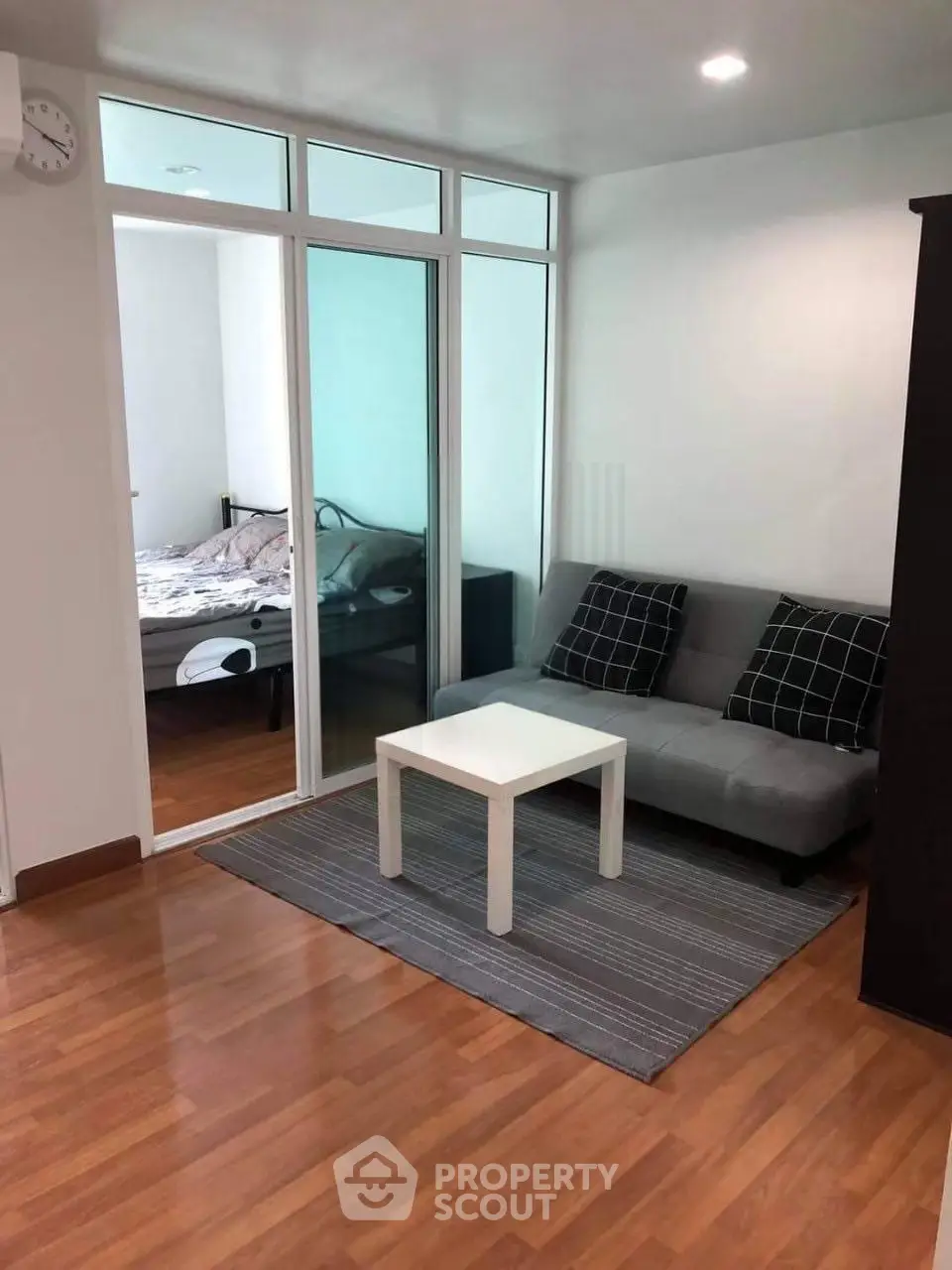 Modern living room with wooden flooring and glass partition leading to bedroom