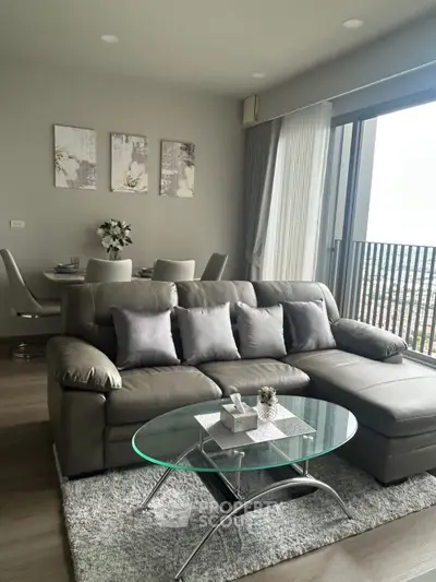 Modern living room with stylish gray sofa and glass coffee table, featuring a balcony view.