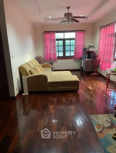 Spacious living room with wooden flooring and large windows, featuring a comfortable sofa and vibrant curtains.