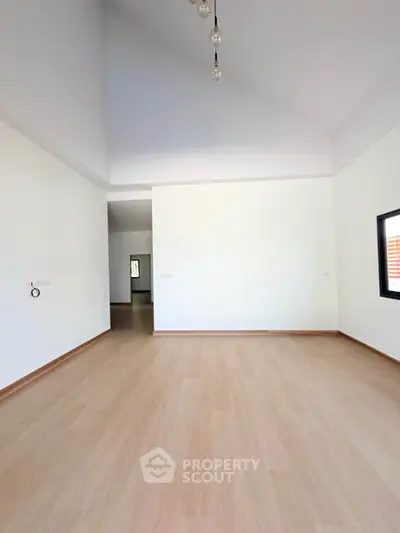 Spacious empty room with high ceiling and wooden flooring, perfect for customization.