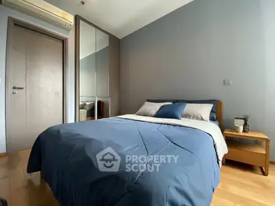 Modern bedroom with blue bedding, mirrored wardrobe, and wooden flooring.