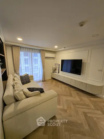 Modern living room with stylish herringbone flooring and large TV setup.