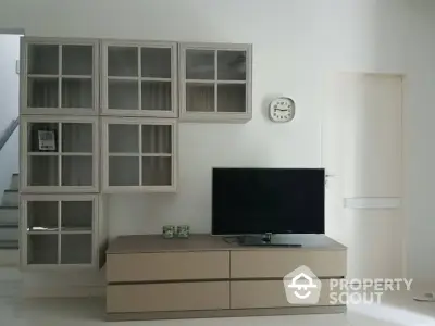 Spacious and well-lit living room with modern minimalist decor, featuring sleek storage units and a large flat-screen TV, perfect for comfortable living.