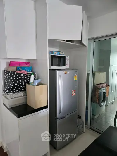 Modern kitchen with sleek fridge and microwave, adjacent to laundry area with washing machine.