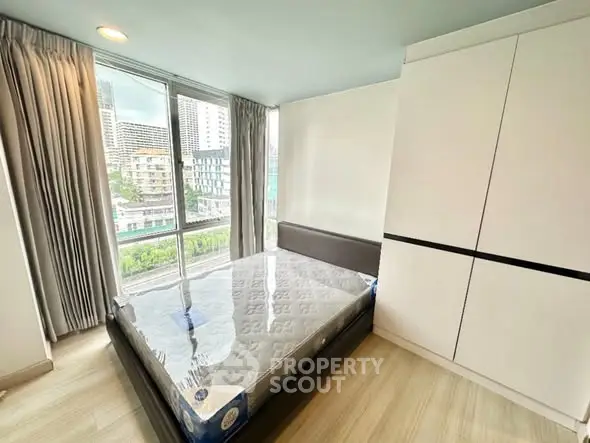 Modern bedroom with large window and city view, featuring a new bed and sleek wardrobe.