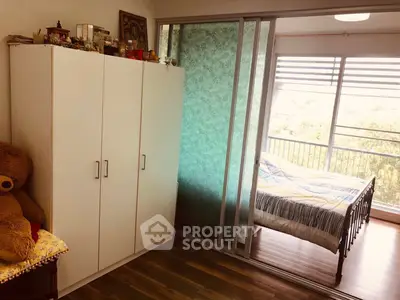 Cozy bedroom with sliding glass doors and balcony view, featuring a wardrobe and wooden flooring.