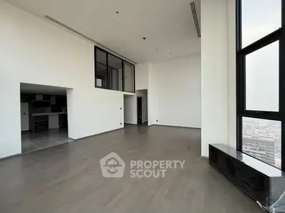 Spacious modern living room with high ceilings and large windows offering city views.