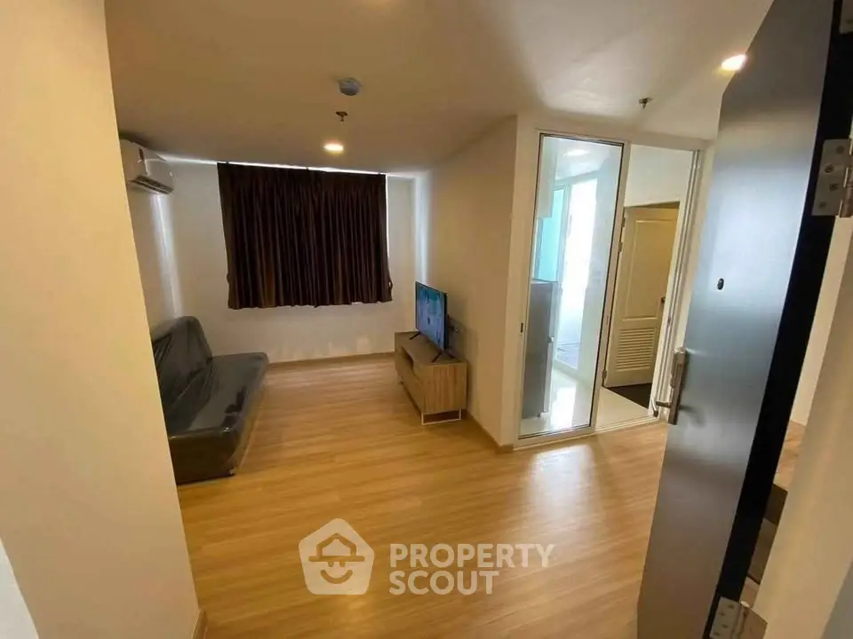 Modern living room with wooden flooring and glass partition, featuring a cozy sofa and TV unit.