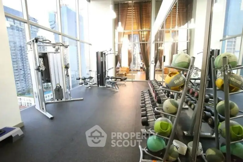Spacious modern gym with city view and fitness equipment in luxury building.
