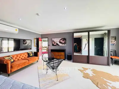 Spacious living room with modern decor, featuring a plush orange sofa, stylish chairs, and large mirrored wardrobe.