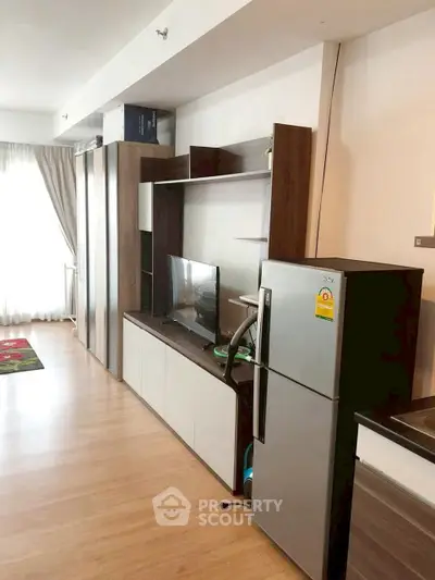 Modern living room with sleek furniture and stainless steel fridge in open layout.