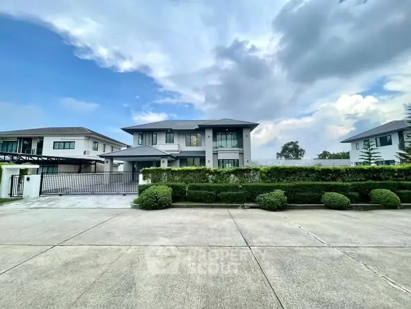 Modern two-story house with lush garden and spacious driveway under a cloudy sky.