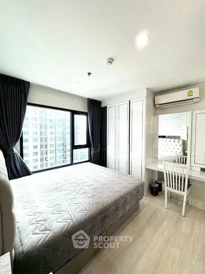 Modern bedroom with large window and stylish decor in urban apartment.