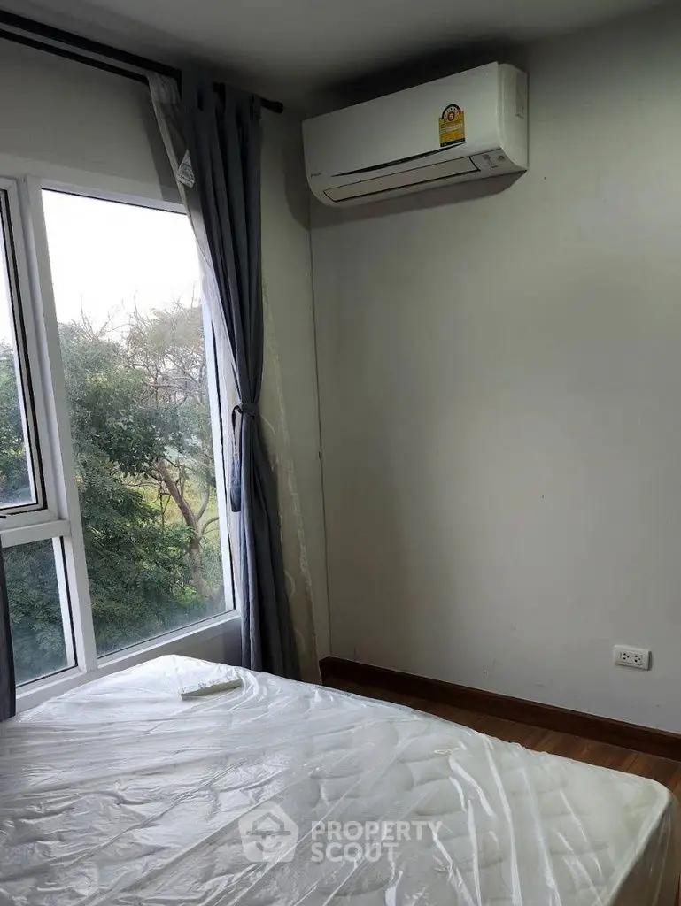 Cozy bedroom with large window and air conditioning, offering a serene view of lush greenery.