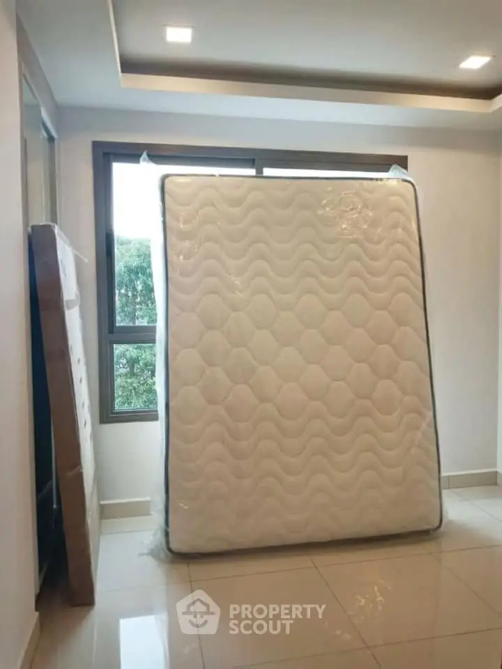 Spacious room with large window and new mattress, ideal for modern living.