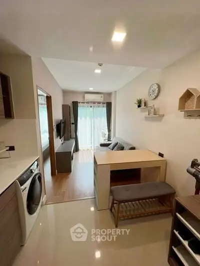 Modern living room with stylish furniture and natural light, featuring a compact washing machine and cozy seating area.